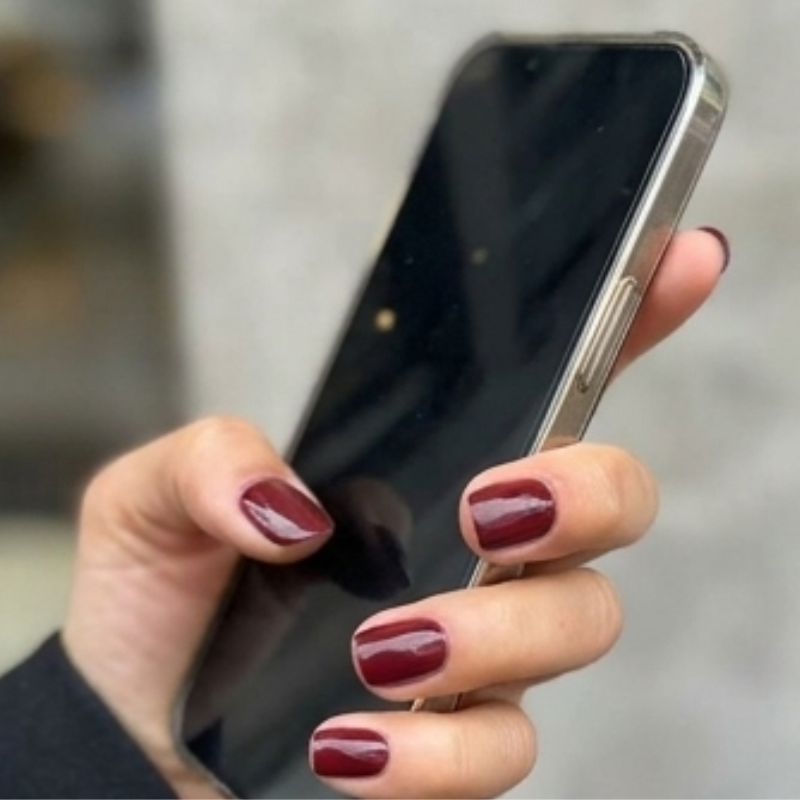 Square Wine & Dine deep red press-on nails holding a phone